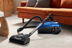 Kirby Signature Series C550 canister vacuum cleaner in Kirby Blue shown sitting on a light beige carpet in a living room setting with an orange sofa in the background.