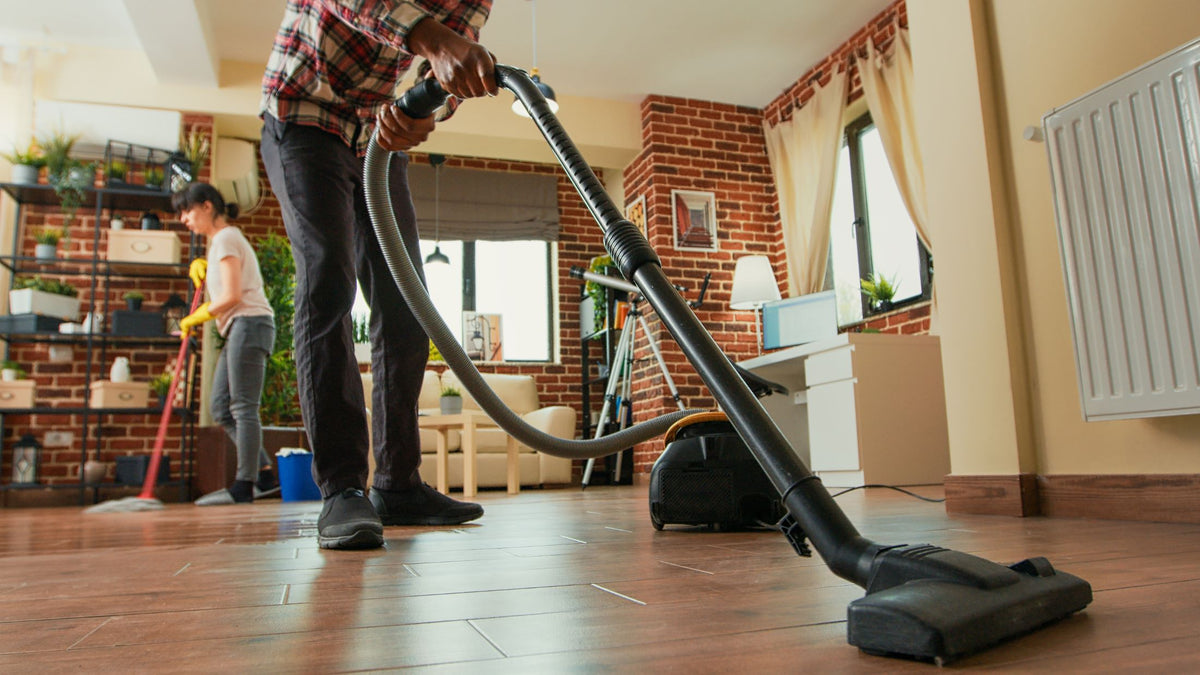 A couple vacuuming the floor and cleaning shelves at home
